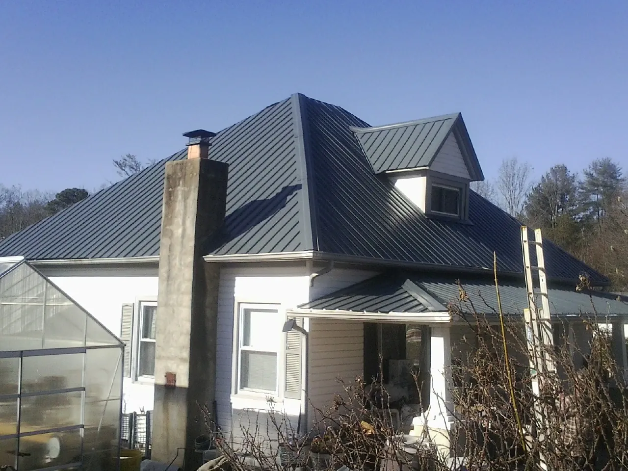 Dark blue standing seam metal roof on a white farmhouse with dormer in Woodstock